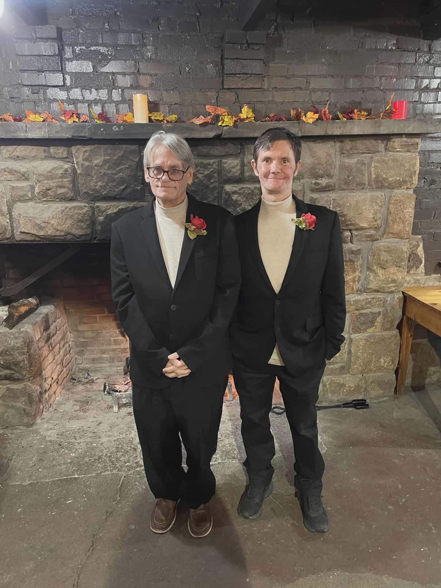 Eddie Harbert and his husband Jason in matching suits with red rose boutonnieres